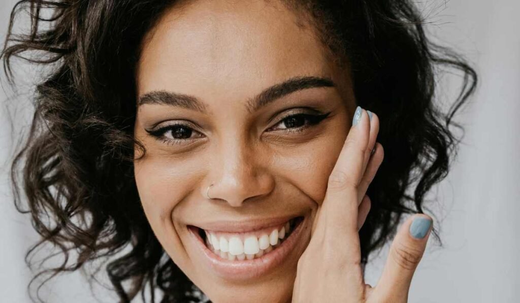 Blog image representing who really needs body butter. Close up image of a woman smiling with hand to her face lovingly.